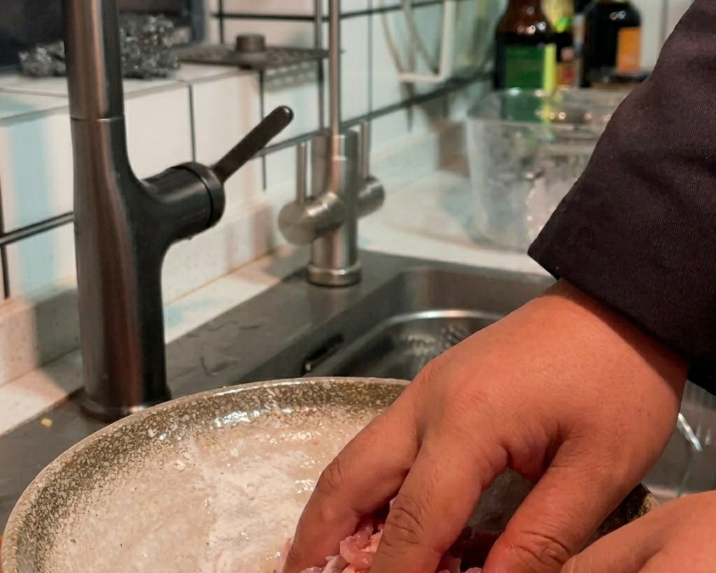 Hand mischt gewürzte rohe Schweinefleischstreifen in einer Schüssel für gleichmäßige Beschichtung.
