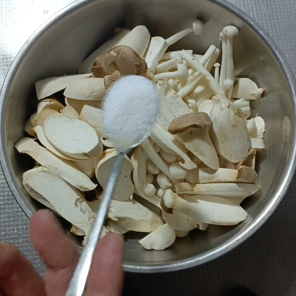 Königs-Austernpilze und Buchenpilze in einer Metallschüssel, die gesalzen werden.