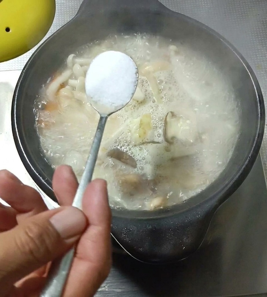 Nahaufnahme eines Löffels, der Gewürze in die kochende Suppe gibt.