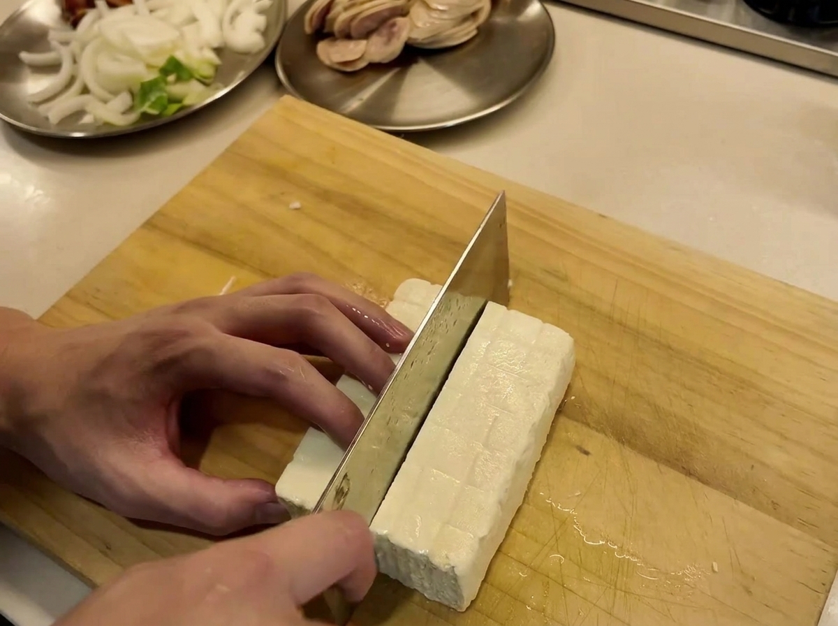 Ein Tofublock wird auf einem Holzschneidebrett in saubere Scheiben geschnitten.