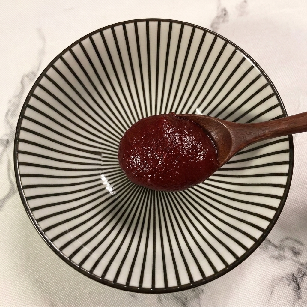 Ein Holzlöffel gibt einen Klecks rote koreanische Chilipaste in eine gemusterte Schüssel.