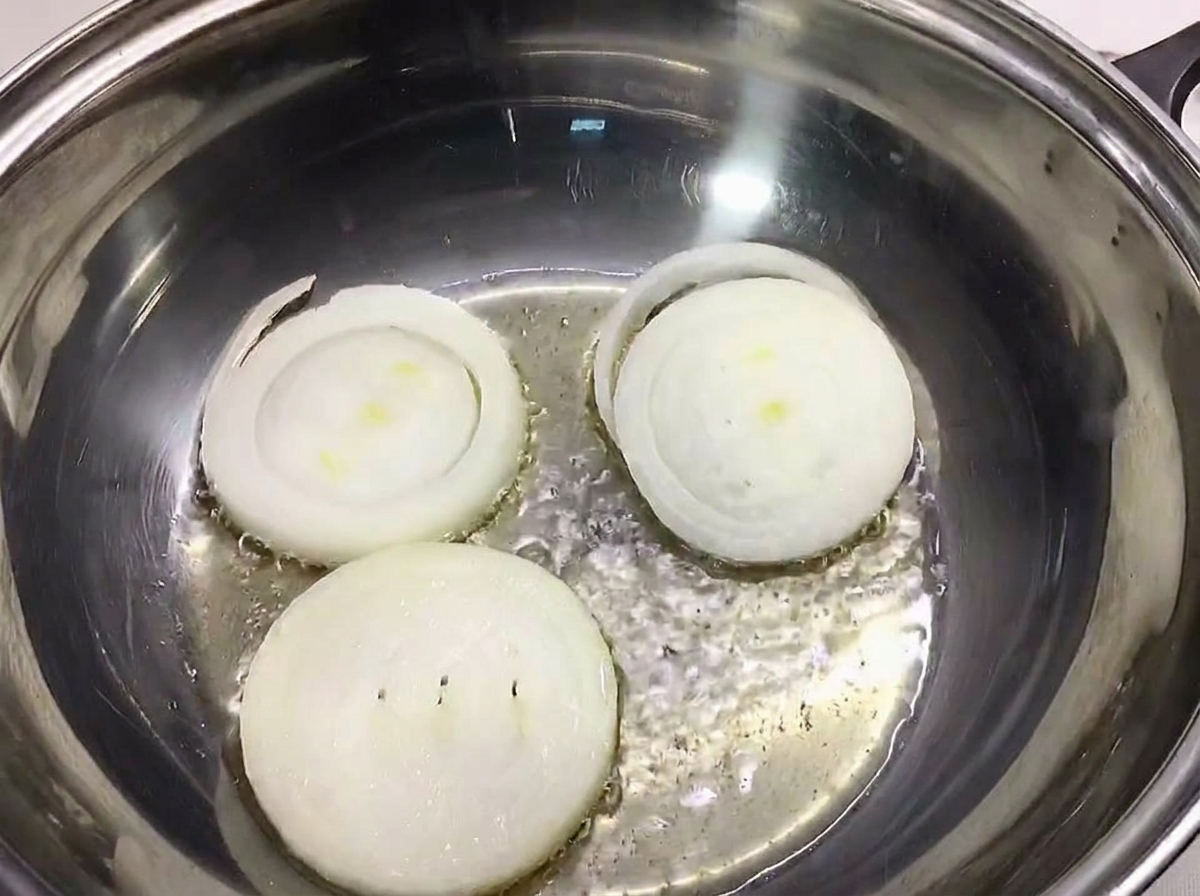 Dicke Zwiebelscheiben liegen auf dem Boden eines Edelstahltopfs.