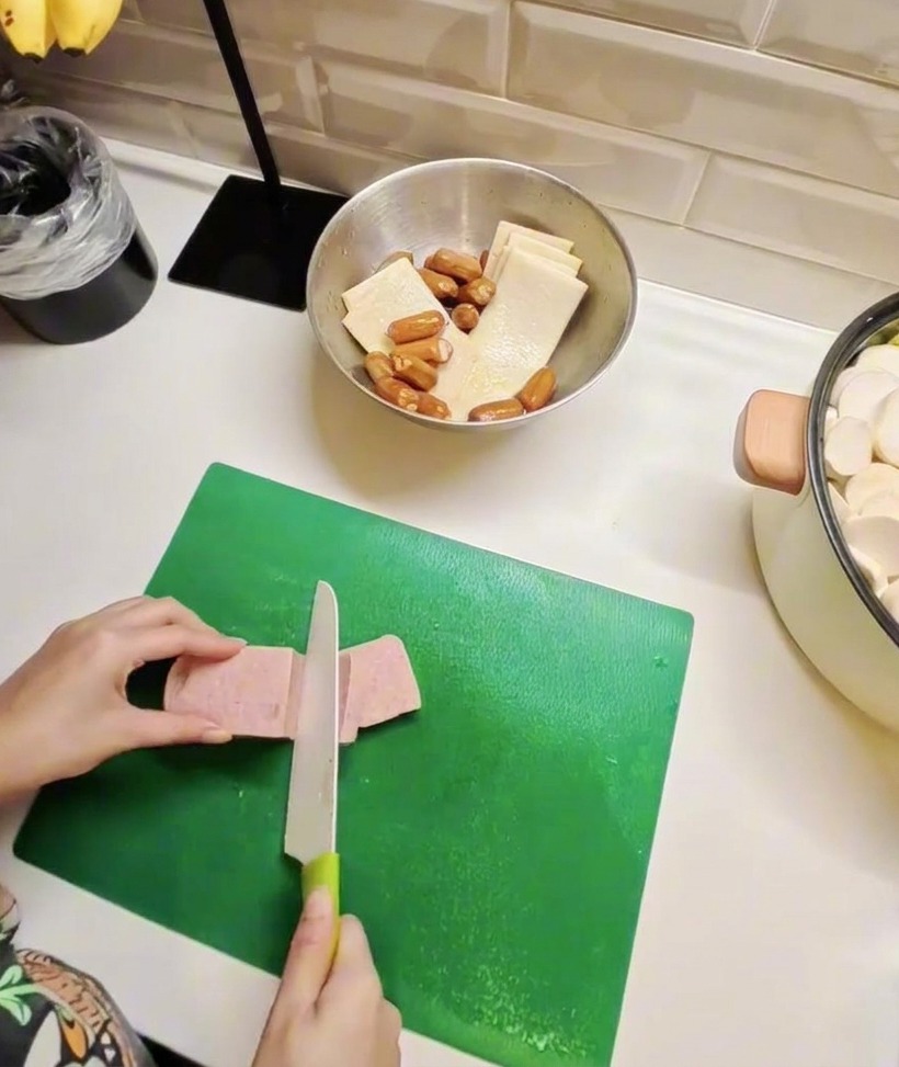 Scheiben von Frühstücksfleisch und Fischkuchen auf einem Brett, um die Vorbereitung der Hauptzutaten zu zeigen.