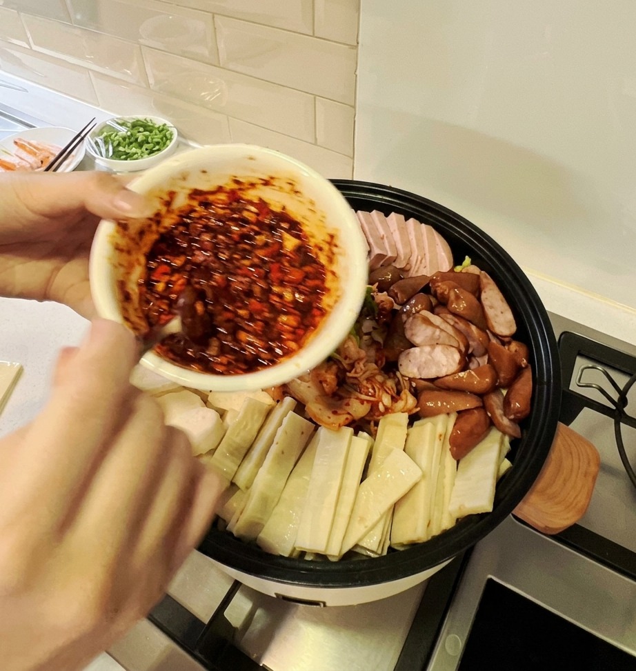 Eine Schale mit leuchtend roter scharfer Sauce wird über die bunten Zutaten in einem großen Eintopftopf gegossen.