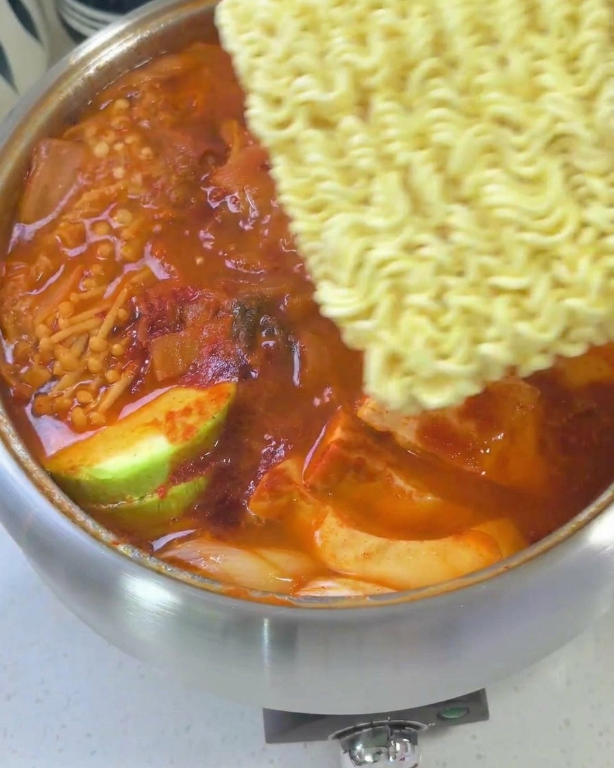 Ein fast fertiger Armee-Eintopf, belegt mit Ramen-Nudeln, Käsescheiben und einem Ei.