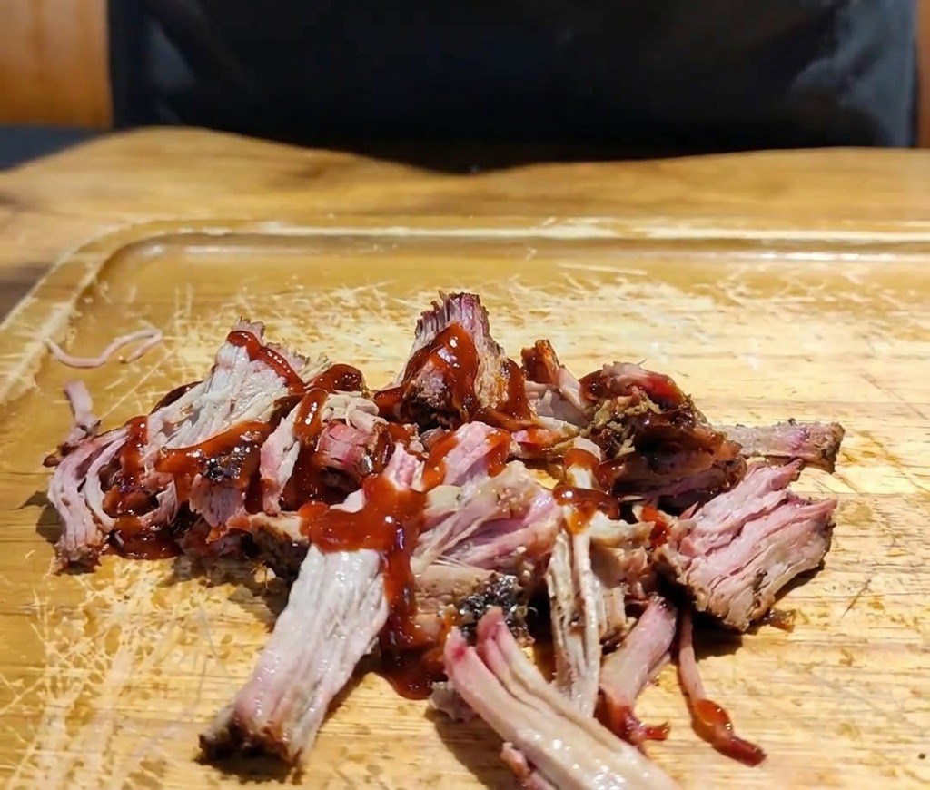 Eine Hand gibt eine Mischung aus geraspeltem Rot- und Weißkohl auf das mit Sauce marinierte Pulled Pork.