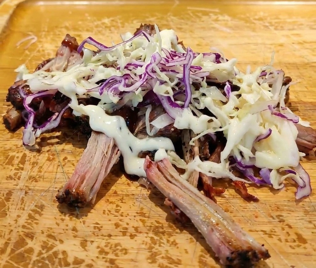 Zerzupftes Schweinefleisch mit BBQ-Sauce, getoppt mit frischem Coleslaw und einem Klecks cremigen weißen Dressings.