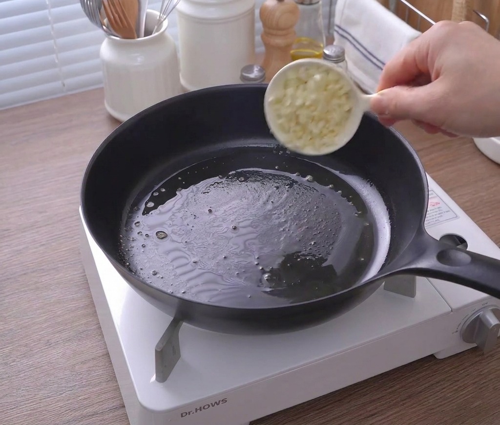 Gehackter Knoblauch wird aus einer kleinen Tasse in die Pfanne mit geschmolzener Butter gegeben.