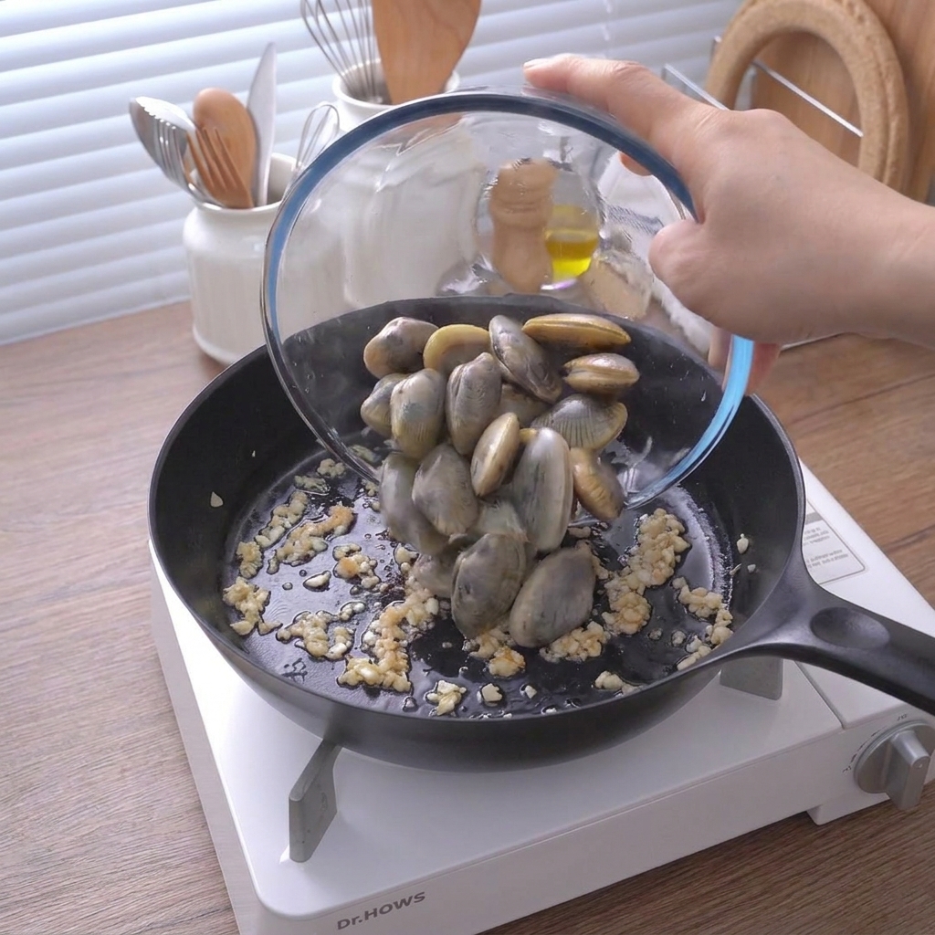 Frische Muscheln werden aus einer Glasschüssel in die Pfanne zu dem Knoblauch gegeben.