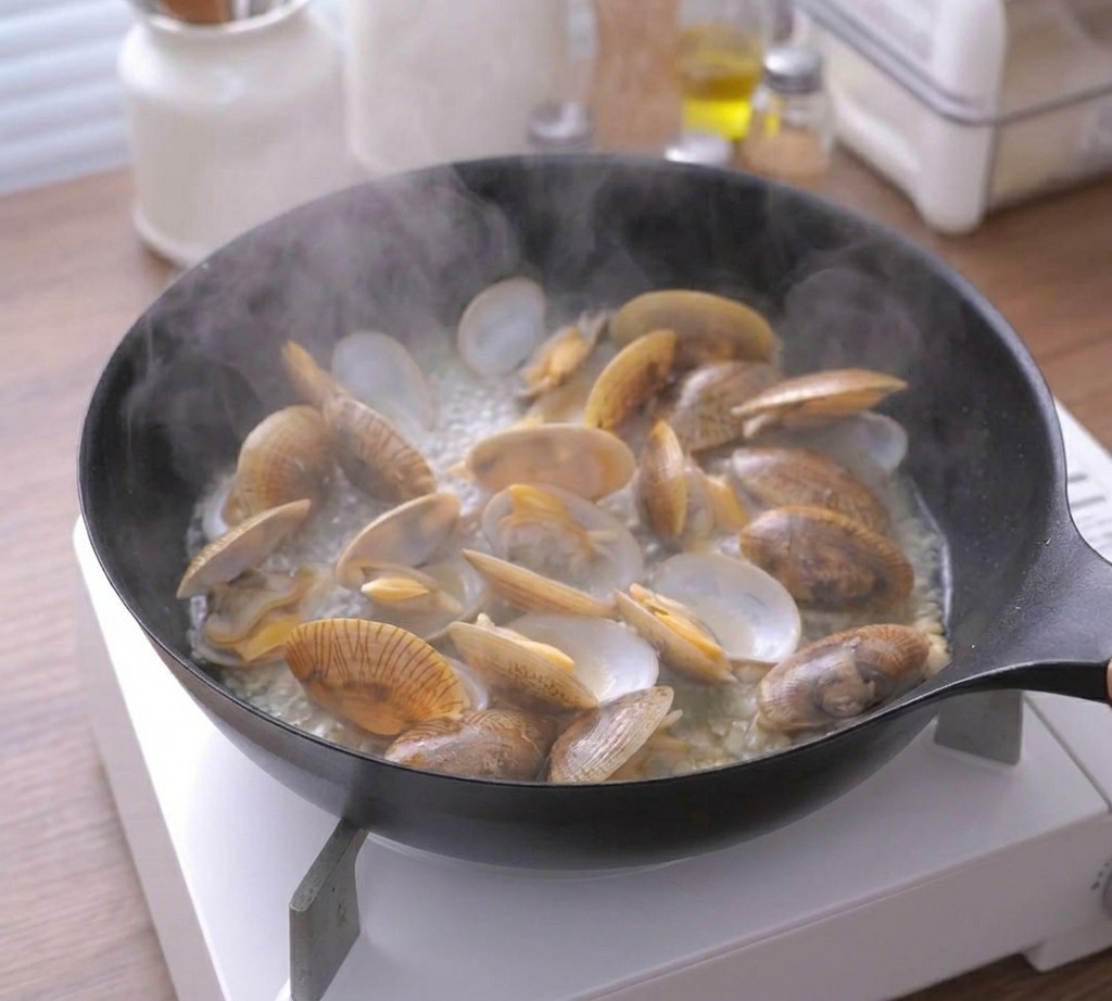 Dampf steigt aus einer Pfanne mit vielen vollständig geöffneten und gegarten Muscheln auf.