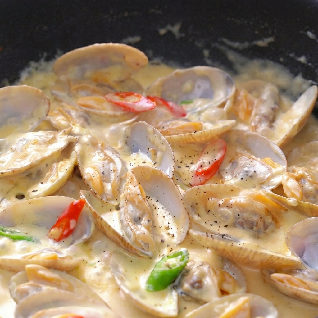 Nahaufnahme von Muscheln in dicker Sahnesauce, garniert mit Pfeffer, Petersilie und Chili.