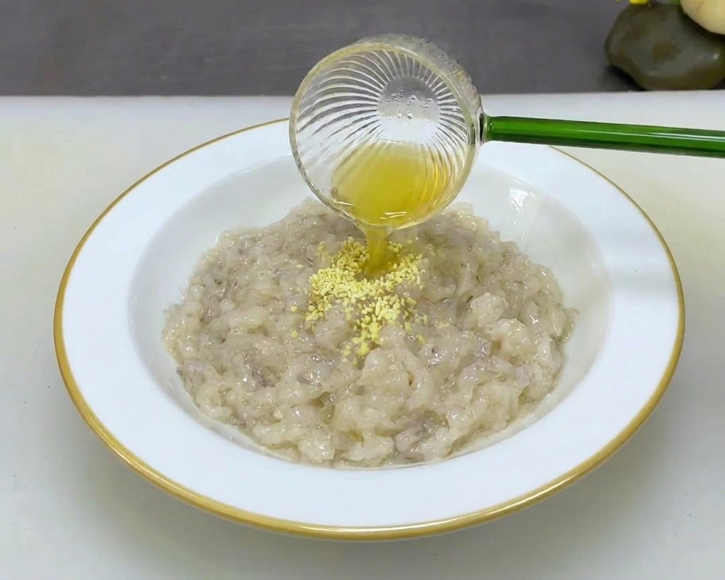 Jemand gibt feines, gelbes Gewürzpulver aus einem Glaslöffel in eine weiße Schüssel mit dicker Garnelenpaste.