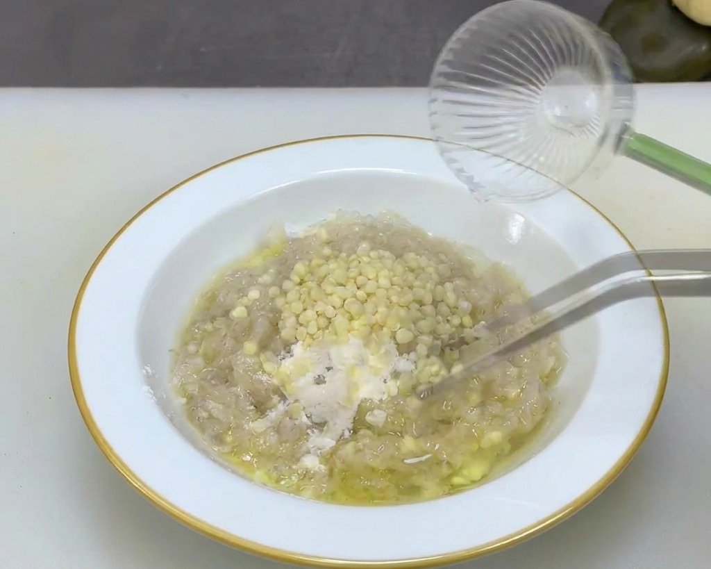 Eine Metallpinzette rührt kleine, runde, cremefarbene Okrasamen in eine helle Garnelenpaste in einer Schüssel.