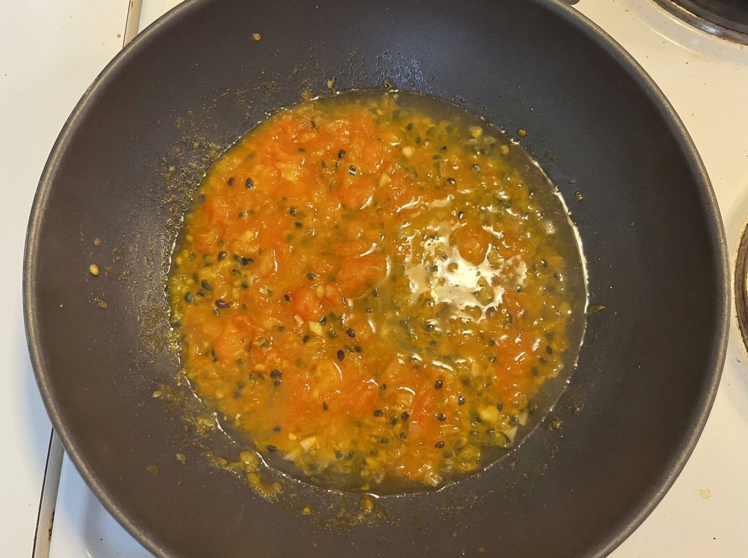 Wasser wird zur Mischung im Wok gegossen, wodurch eine leuchtend orangefarbene Brühe mit Passionsfruchtkernen entsteht.