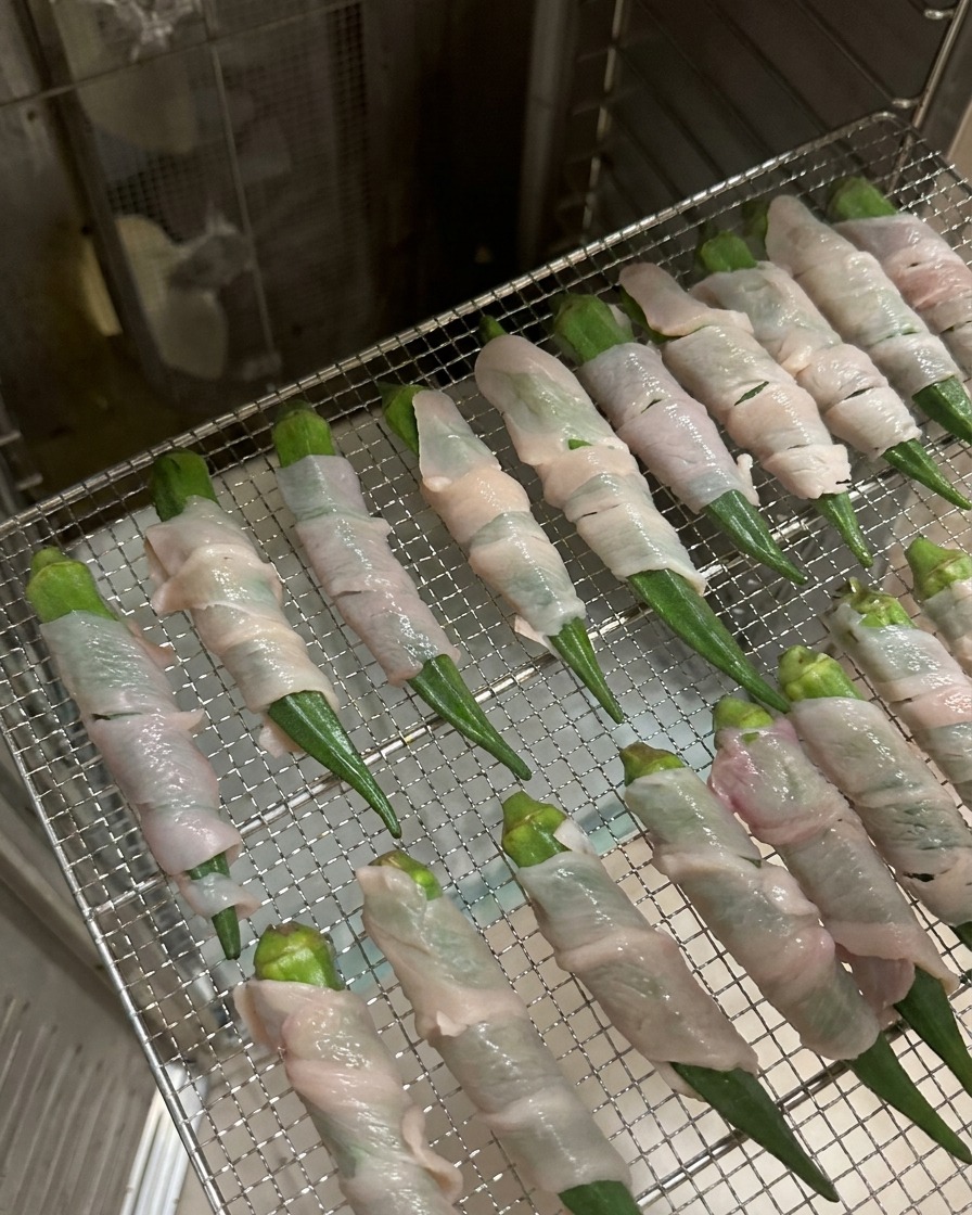 Reihen von mit Hähnchen umwickelten Okraschoten auf einem Metallgitter in einem Dörrautomaten aus Edelstahl.