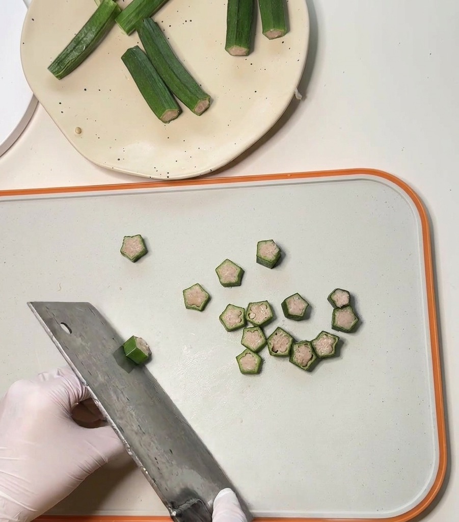 Ein großes Metallbeil schneidet gefüllte Okraschoten in kleine, sternförmige Scheiben für Haustier-Leckerlis.