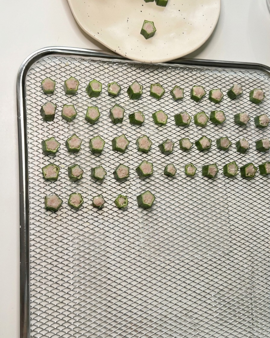Dutzende sternförmige Okra-Hähnchen-Leckerlis sind in ordentlichen Reihen auf einem Gitterrost eines Dörrgeräts angeordnet.