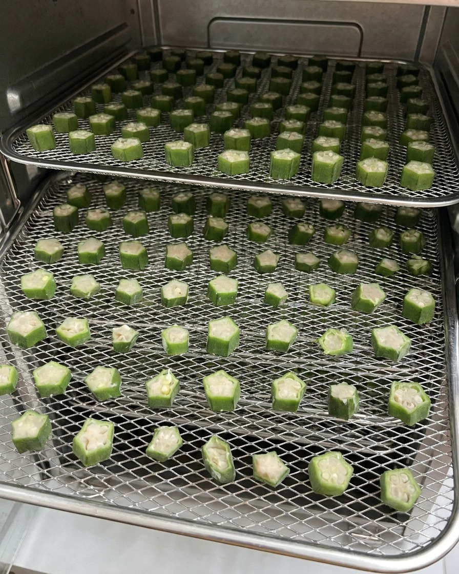 Zwei mit Okra-Hähnchen-Snacks gefüllte Gitterroste befinden sich während des Trocknungsprozesses in einem Dörrautomaten.