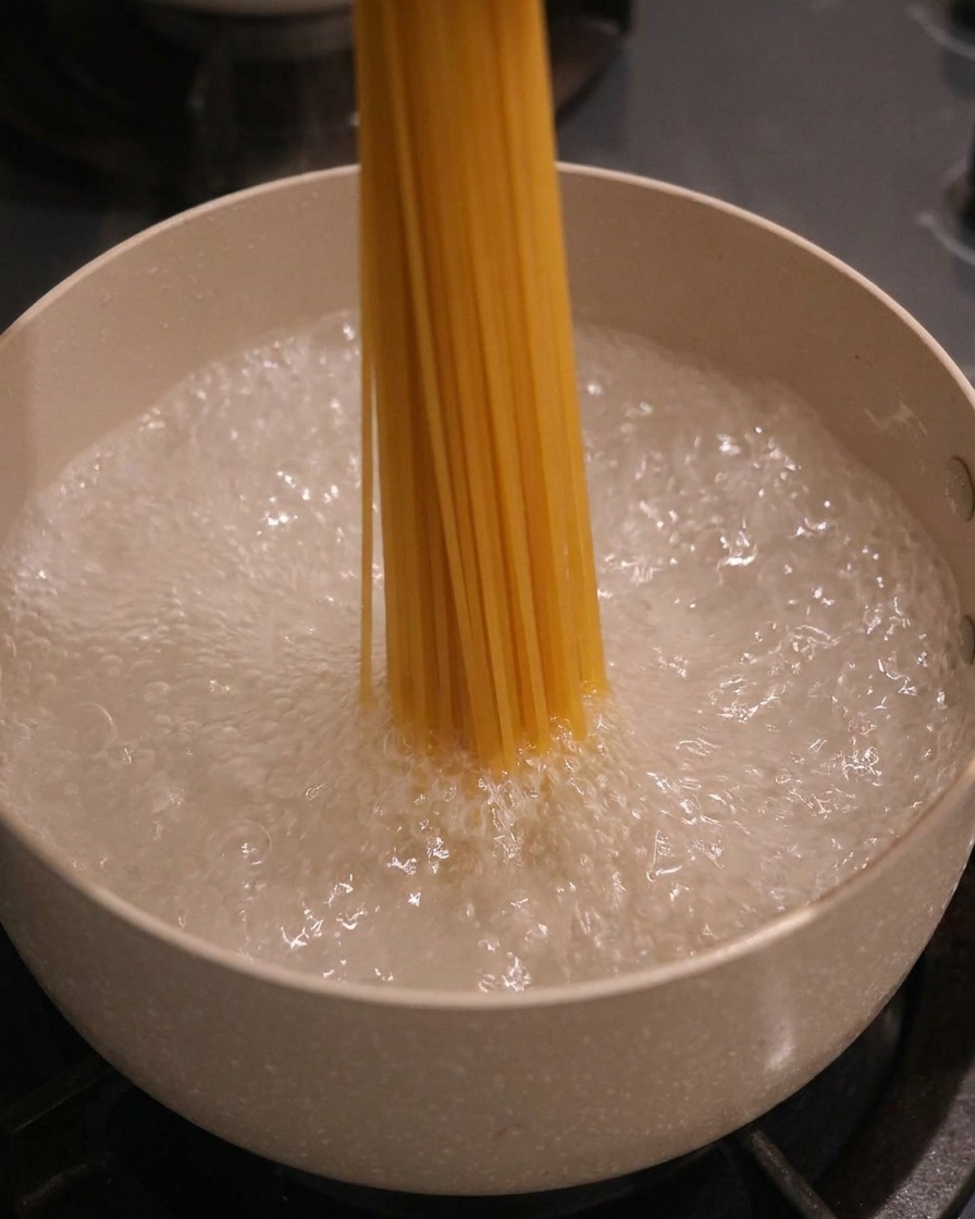 Ein Bündel trockene Spaghetti wird vertikal in einen Topf mit kochendem Wasser gegeben.