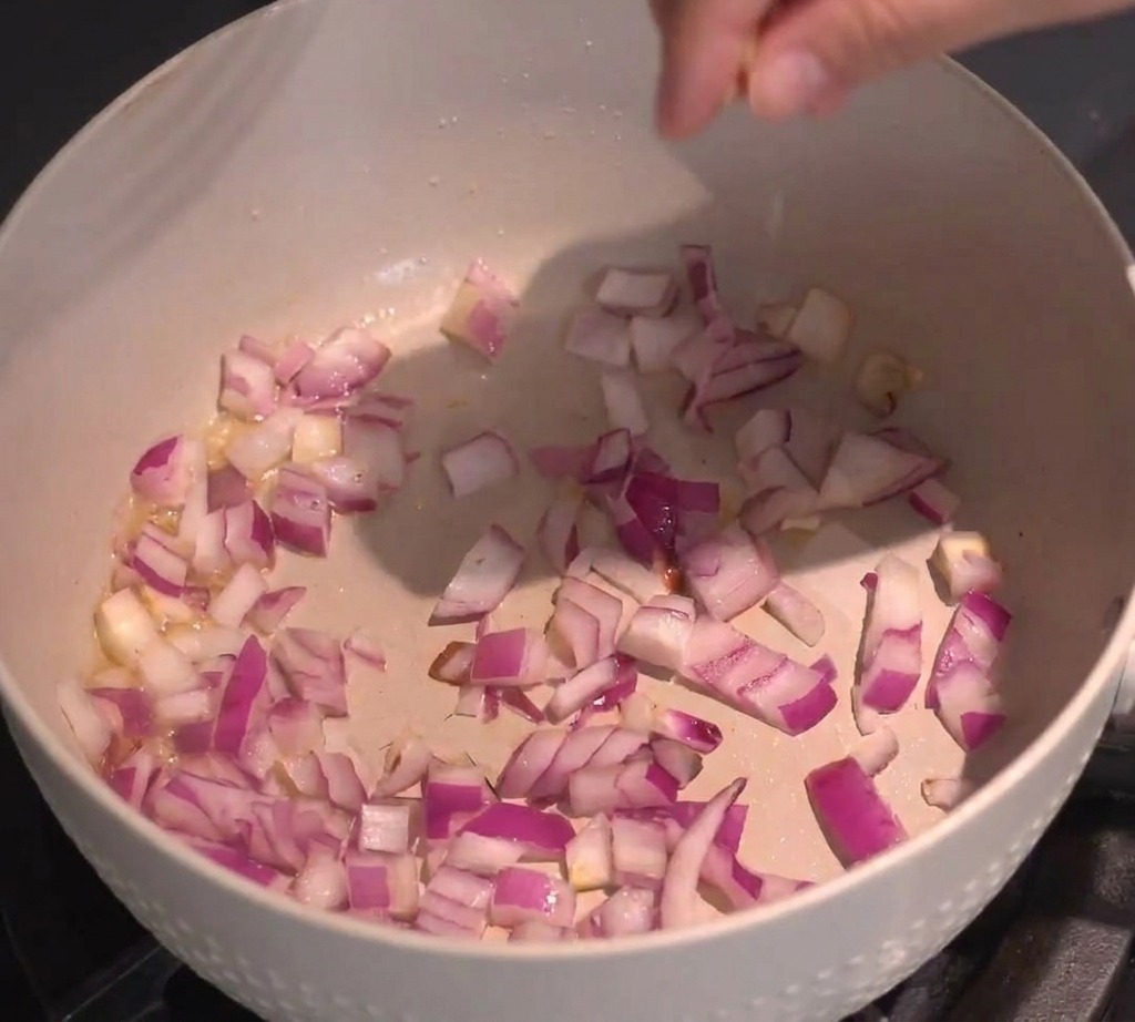 Gewürfelte rote Zwiebeln werden in einer Pfanne auf dem Herd angebraten.