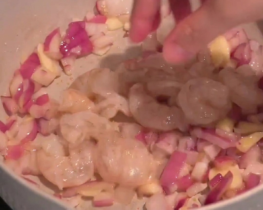 Rohe Garnelen werden zu den Zwiebeln und dem Knoblauch in die Pfanne gegeben.