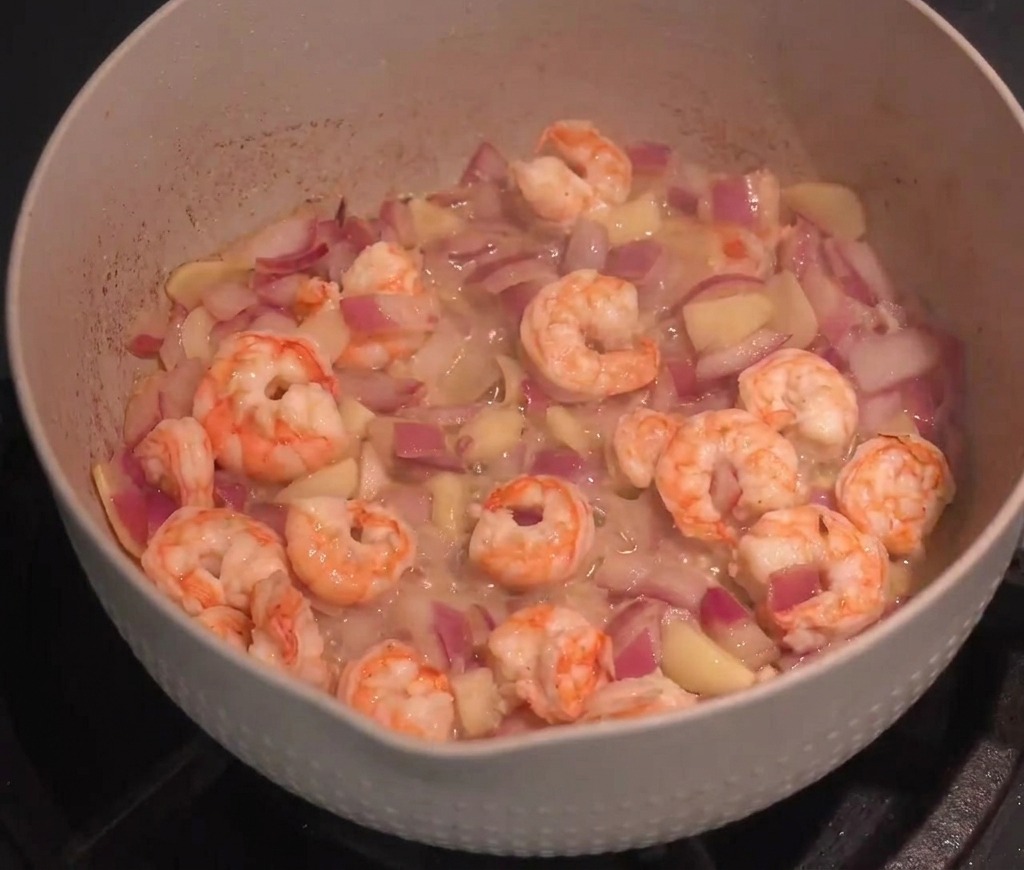 Garnelen werden mit Zwiebeln und Knoblauch in einer Pfanne pfannengerührt.