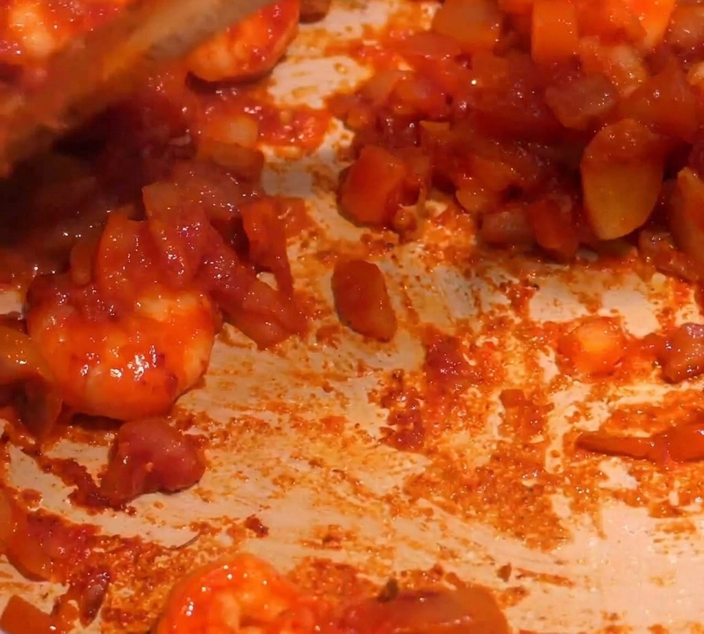 Eine dicke, rote Garnelensauce wird in einer Pfanne gerührt, während Flüssigkeit hinzugefügt wird.