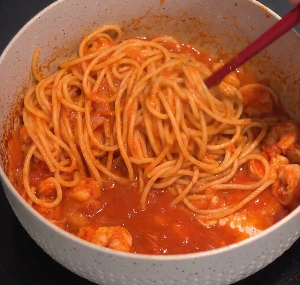 Spaghetti werden mit einer Küchenzange in einer dunklen Sauce geschwenkt.