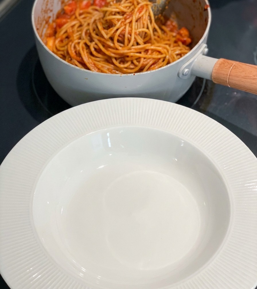 Ein Topf mit fertiger Pasta steht neben einer leeren weißen Schüssel.
