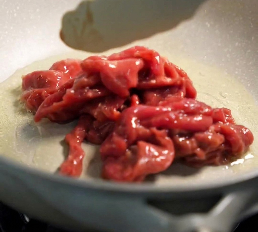 Eine Zange legt mariniertes Rindfleisch in eine heiße Pfanne mit Öl.