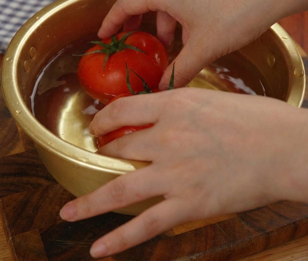 Zwei ganze rote gefrorene Tomaten werden in einer goldenen Metallschüssel mit Wasser eingeweicht.