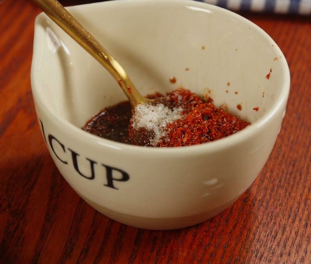 Rote Sauce mit Chilipaste und Gewürzen wird in einer kleinen Keramiktasse mit einem goldenen Löffel verrührt.