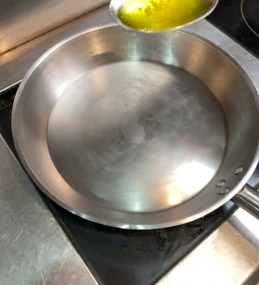 Ein Löffel gießt goldenes Speiseöl in eine saubere, erhitzte Edelstahlpfanne.