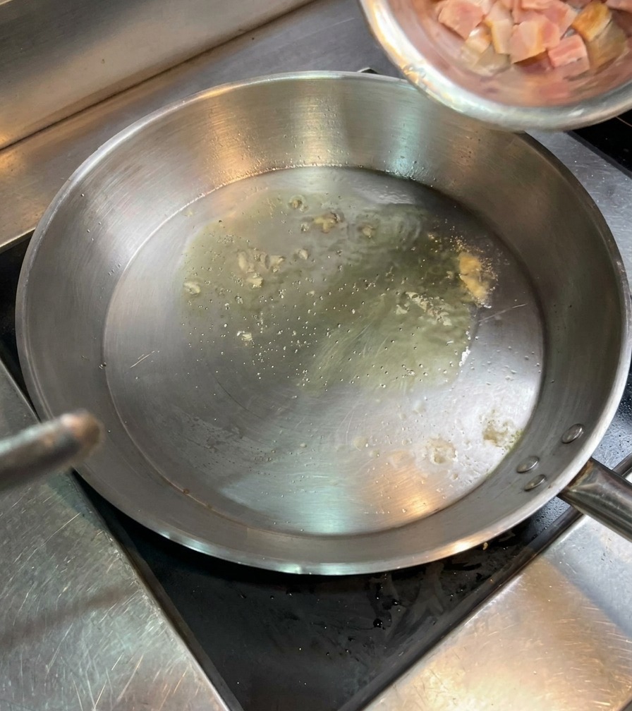 Rohe Speckwürfel werden aus einer Schale in eine Pfanne mit heißem Öl geschüttet.