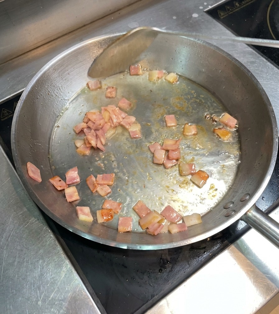 Speckwürfel braten goldbraun in der Pfanne und werden mit einem Pfannenwender bewegt.