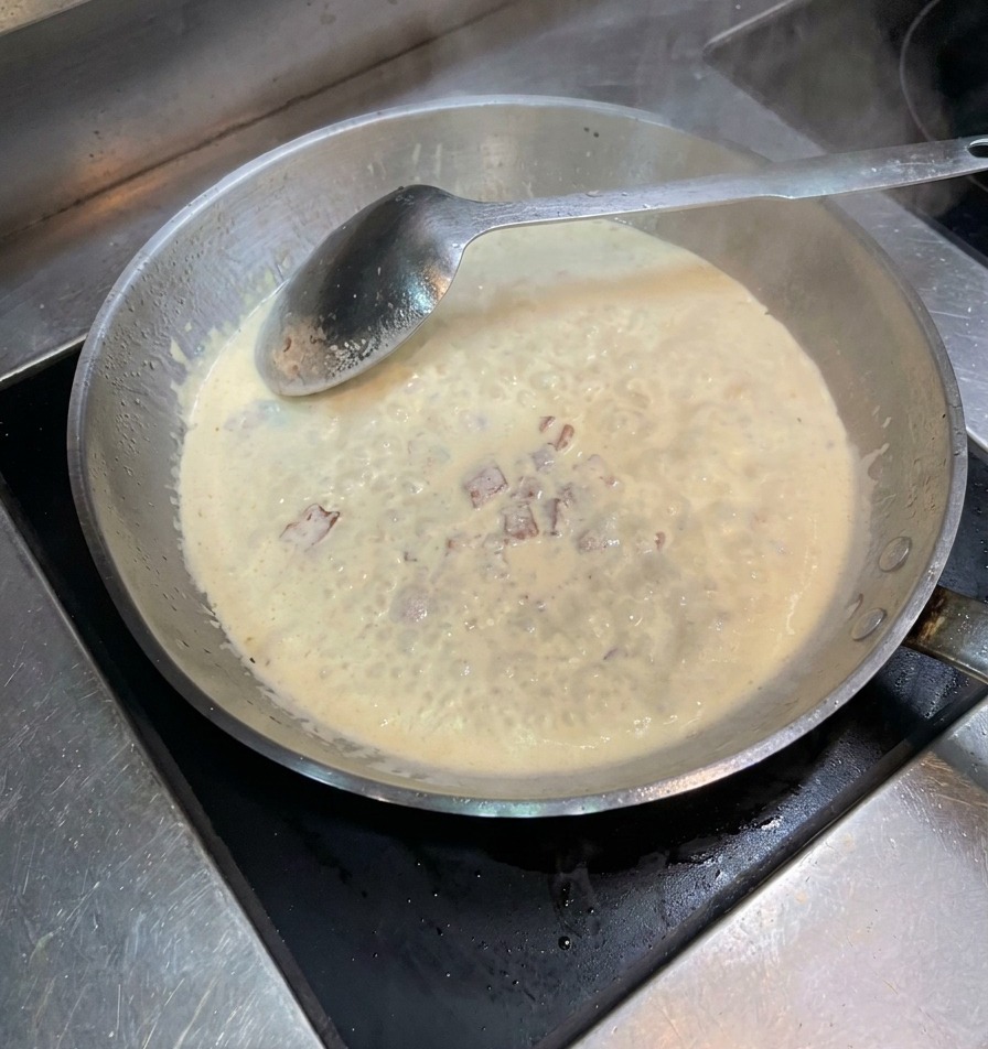 Salz und Pfeffer werden über die köchelnde Sahne-Speck-Soße gestreut.