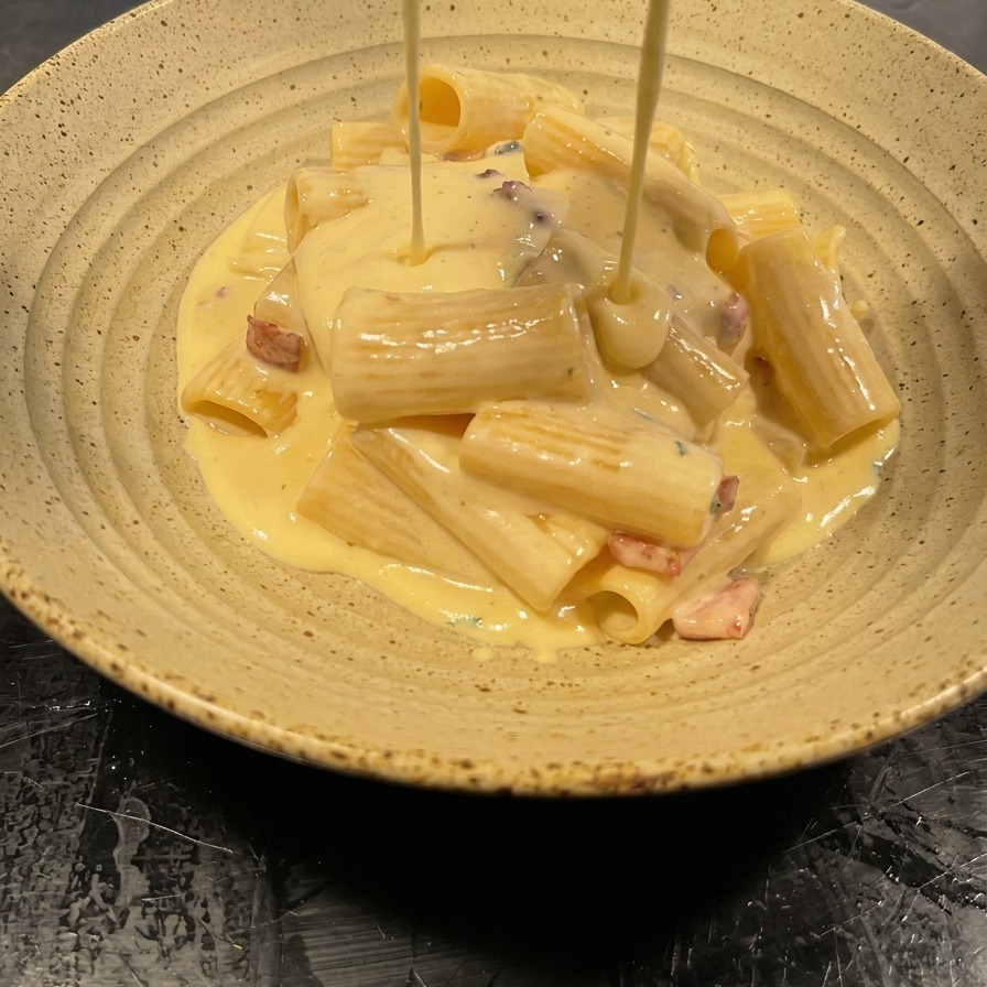 Dicke, samtige Sahnesoße wird aus der Pfanne über die angerichteten Rigatoni gegossen.