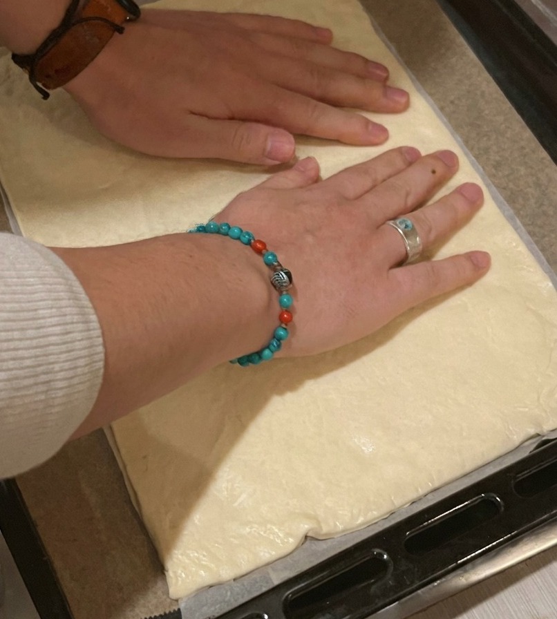 Eine Person legt einen rechteckigen Pizzateig auf ein mit Backpapier ausgelegtes schwarzes Backblech.