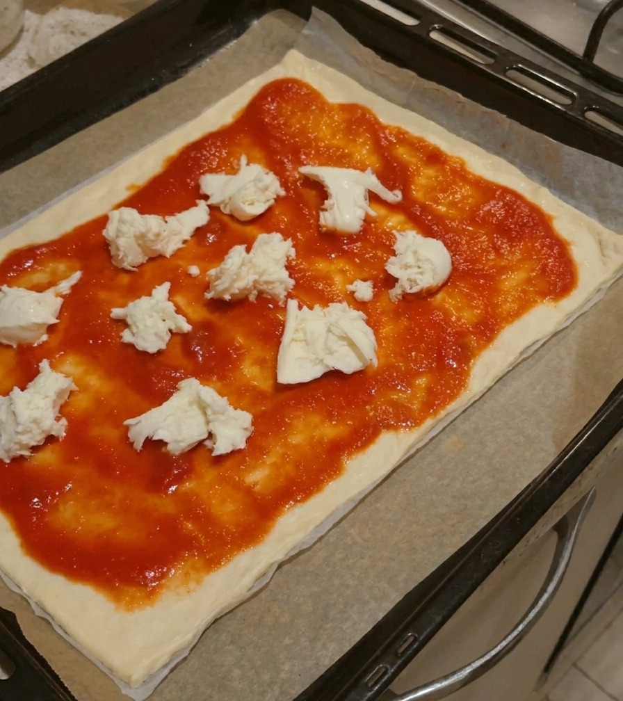 Große Stücke frischer weißer Mozzarella liegen auf der Tomatensauce auf einem Pizzaboden.
