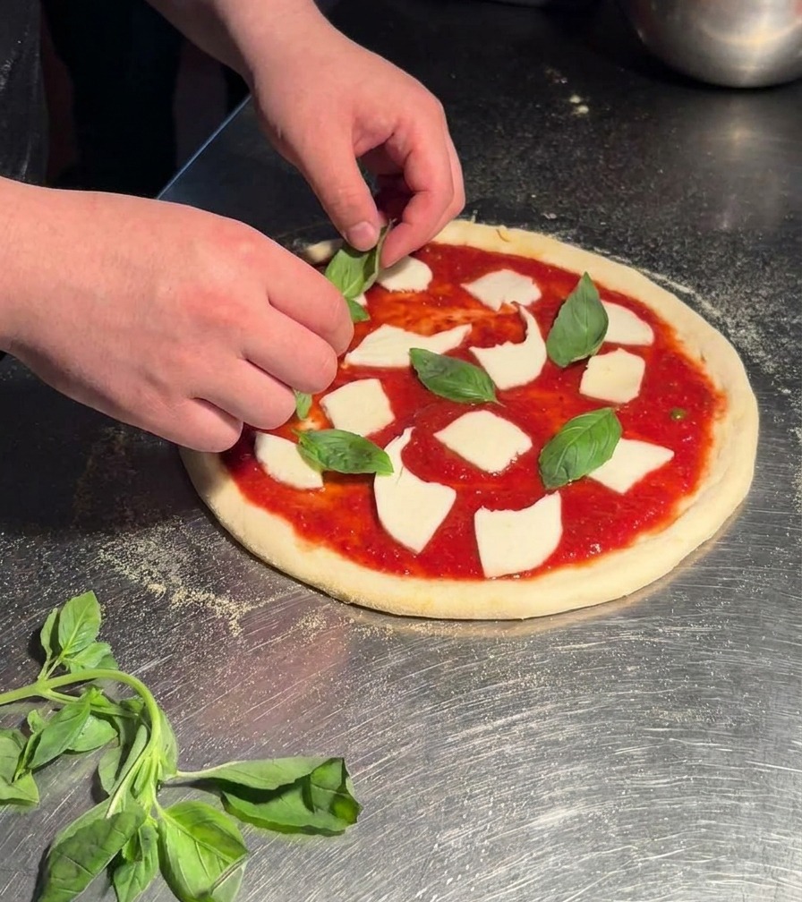 Hände legen frische, grüne Basilikumblätter auf eine rohe Pizza Margherita.