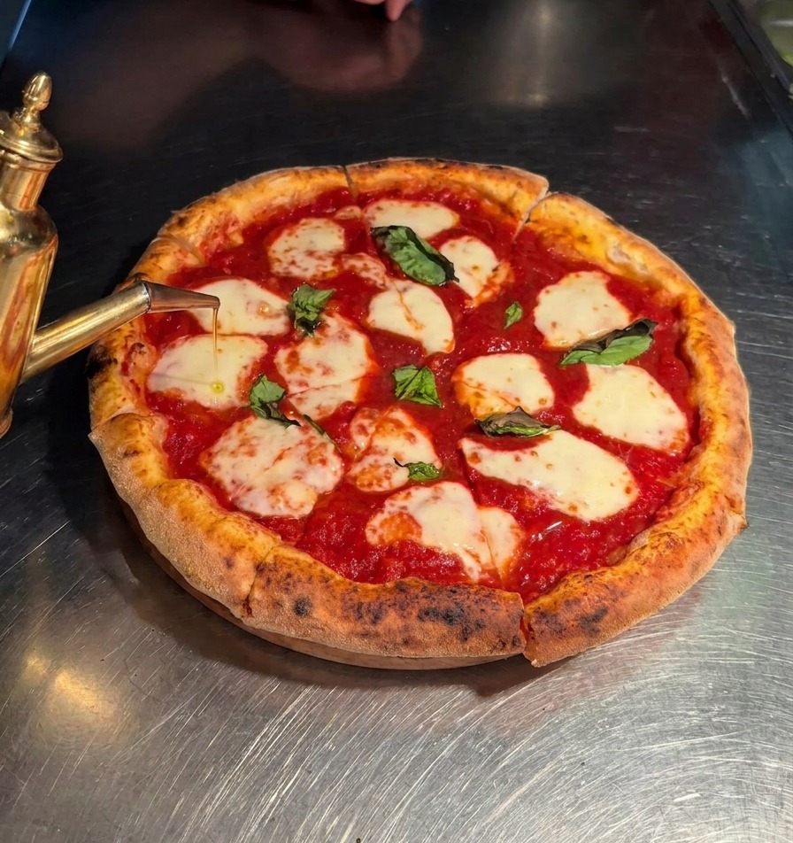 Natives Olivenöl extra wird aus einer Kanne über die geschnittenen Pizzastücke gegossen.