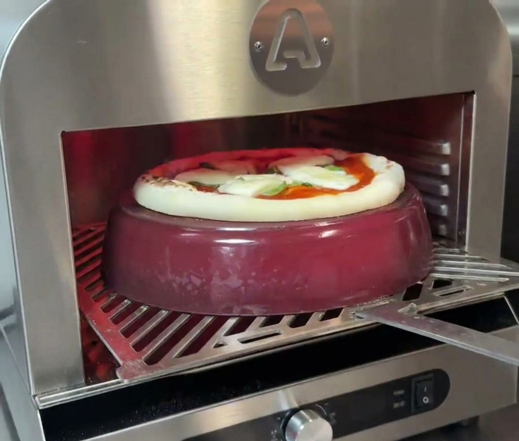 Eine Pizza backt auf einem Gusseisentopf; der Rand beginnt sichtbar aufzugehen und zu bräunen.