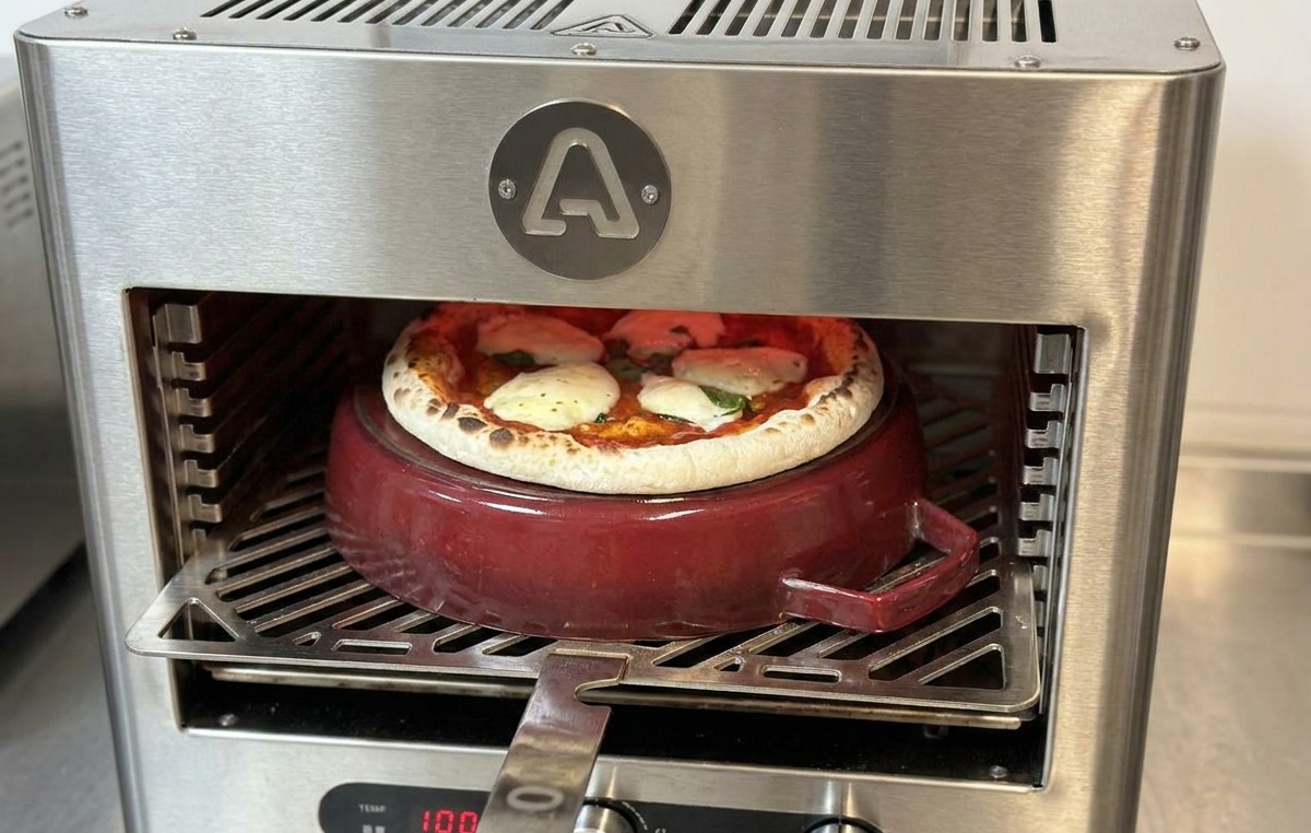 Ein Pizzaschieber wird in den Ofen eingeführt, um eine fast fertige Pizza auf dem Topf zu drehen.