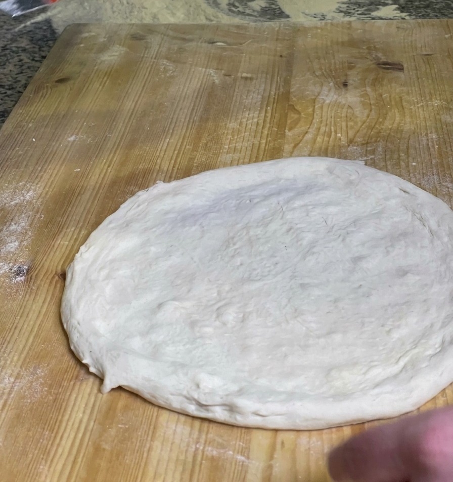 Ein Koch verteilt eine Schicht leuchtend rote Tomatensauce auf der Mitte eines rohen Pizzateigs auf einem Holzbrett.