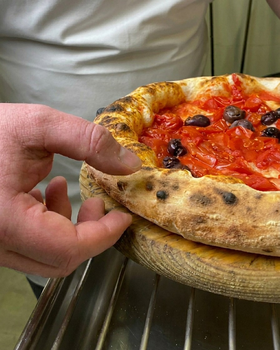 Der Finger eines Kochs drückt in den weichen, gebräunten und aufgegangenen Rand einer frisch gebackenen Pizza Marinara.