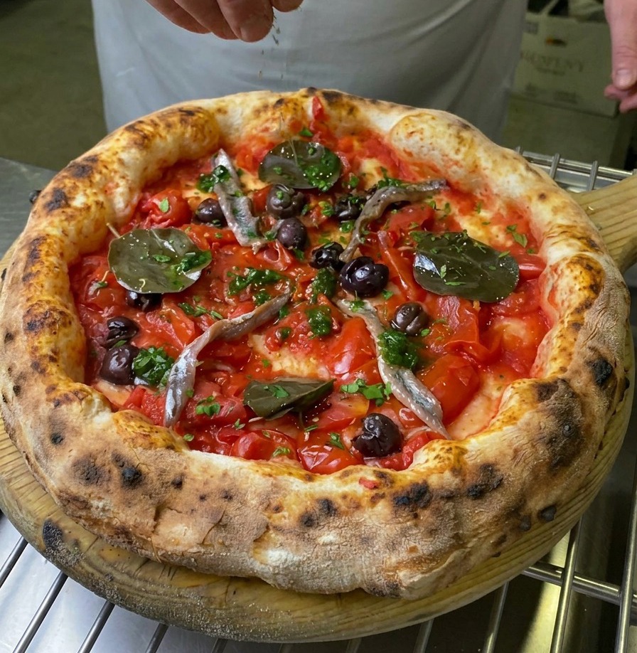 Eine Hand streut frische grüne Kräuter über die Mitte einer gebackenen Pizza Marinara.