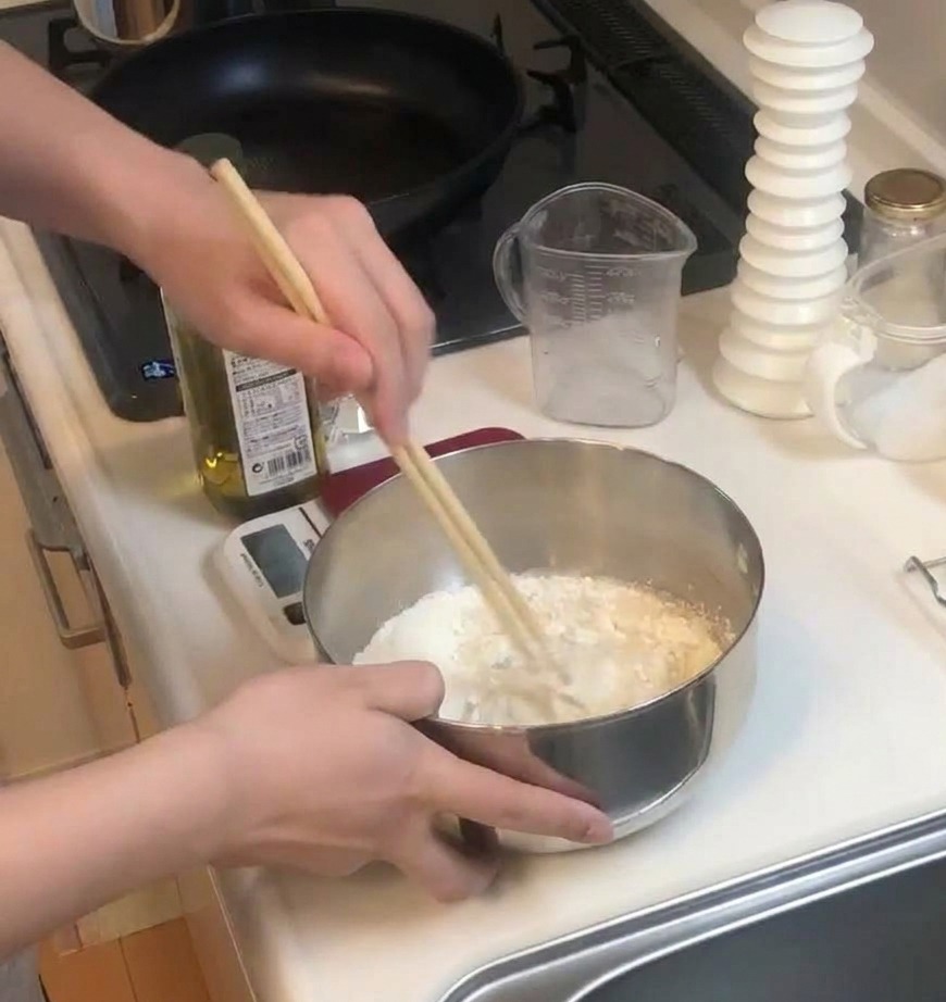 Eine Person rührt mit zwei Holzstäbchen kräftig eine Mischung aus Mehl und Flüssigkeit in einer Edelstahlschüssel.