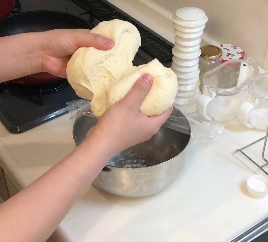 Zwei Hände teilen ein großes Stück weichen Pizzateig in zwei gleich große Abschnitte.