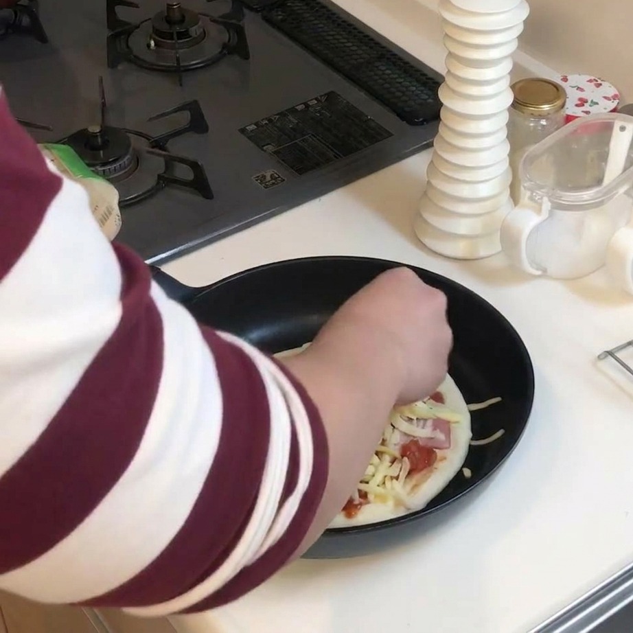 Eine Hand streut eine dicke Schicht geriebenen gelben und weißen Käse über die belegte Pizza in der Pfanne.