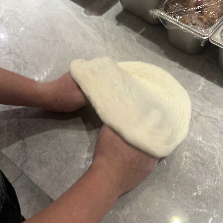 Hände heben und drehen den rohen Pizzateig, um ihn kreisförmig mit einem sichtbaren Rand zu dehnen.